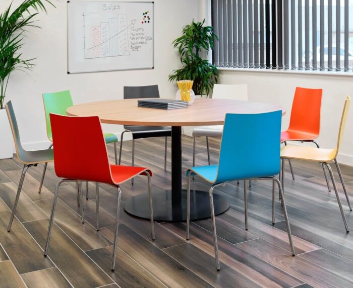 Aurora Meeting Table with oak finish circular top and a single pedestal base in black shown with 8 chairs in a meeting room