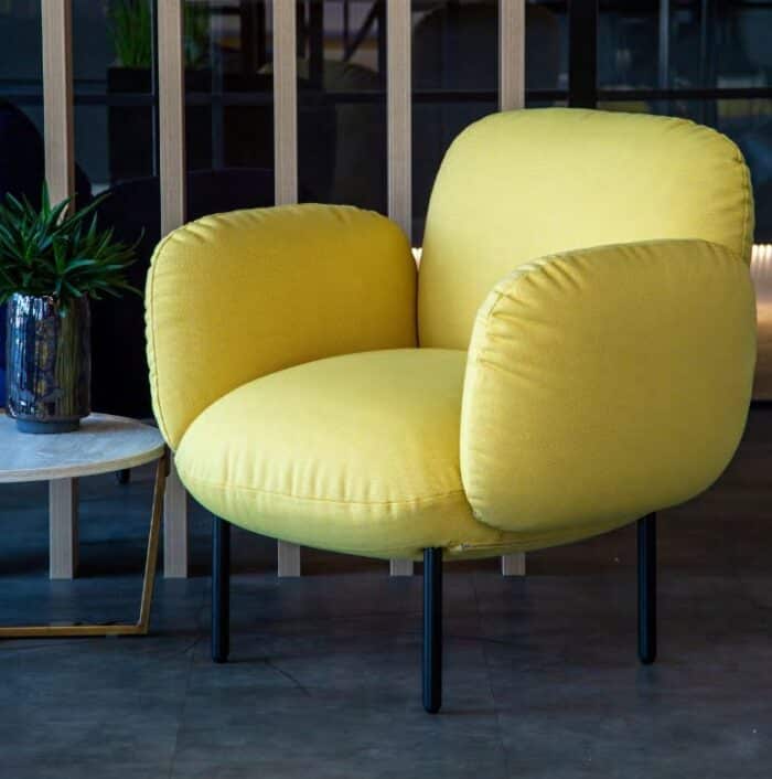 Boho Chair with a black 4 leg frame and yellow upholstery shown in by a coffee table