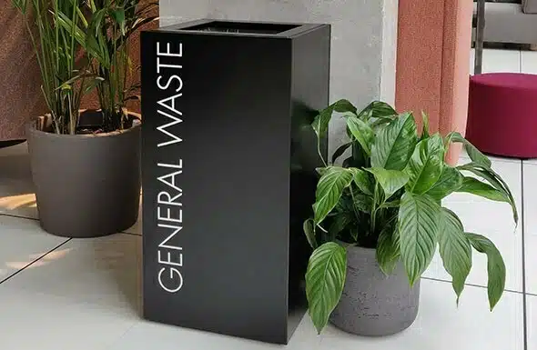 CZ Recycling Bin in black finish shown next to potted plants