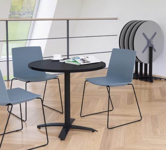 FLIP - Flip Top Table - a circular breakout table wiht three chairs and stacked folded tables against a wall, in a breakout space