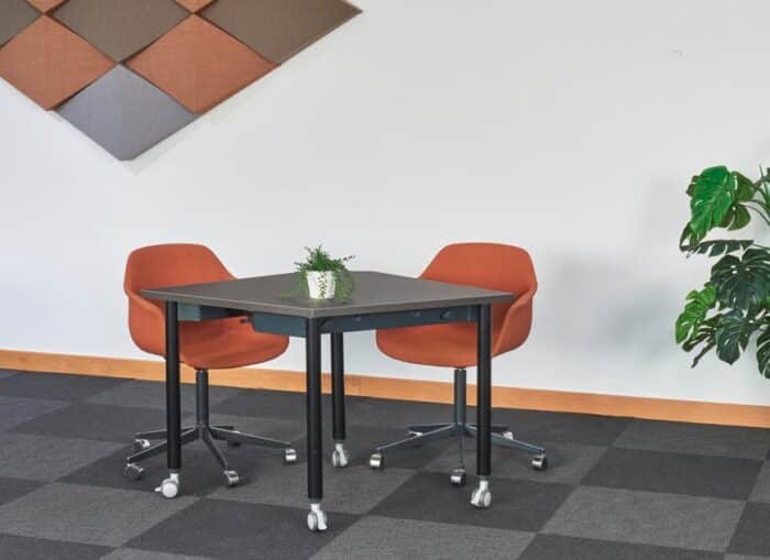 FourKonnect Tables square top table with straight legs in black finish shown with two armchairs in a workplace