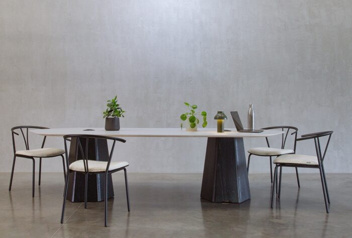 Isle Table with two bases and a shaped rectangular top with optional table top power modules in a two tone finish, shown with four chairs