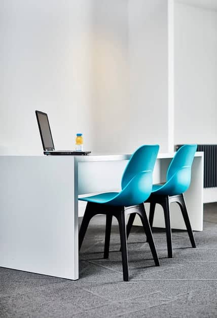 LG4 Plastic Seating two chairs with turquoise plastic shell and black legs shown by a bench desk in a work space