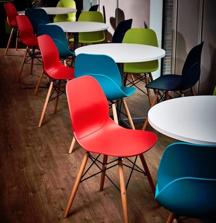LG4 Wood Seating chairs with red , blue and green plastic shells and wood effect legs shown around circular diner height tables
