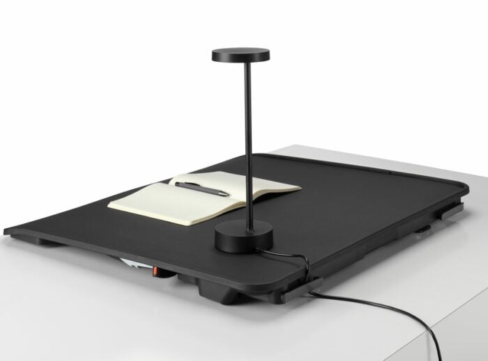 Monto Sit Stand Riser shown in flat position with a notebook and lamp on top
