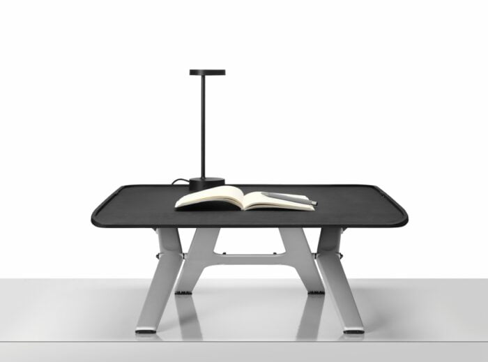 Monto Sit Stand Riser shown in mid height position with a notebook, pen and lamp