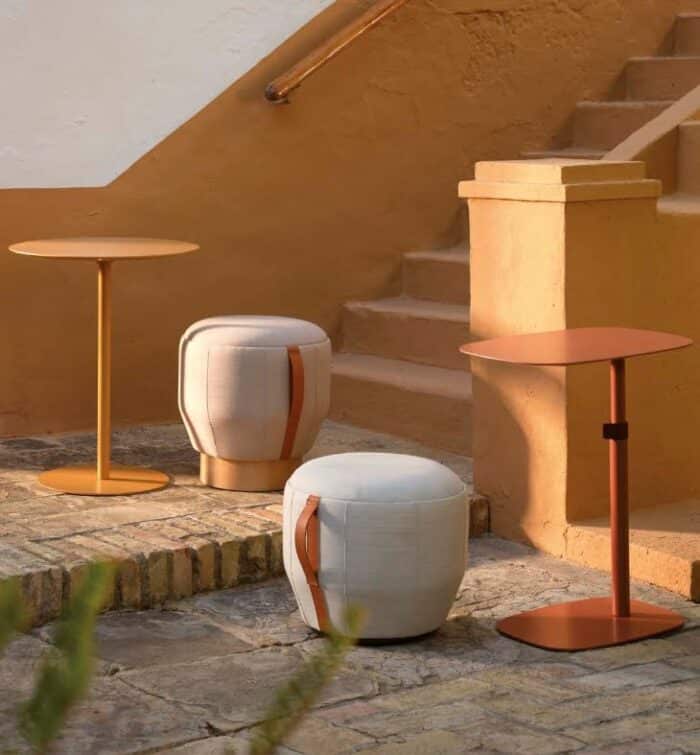 Nota Table a round and a rectangular table shown in an outside space with two poufs