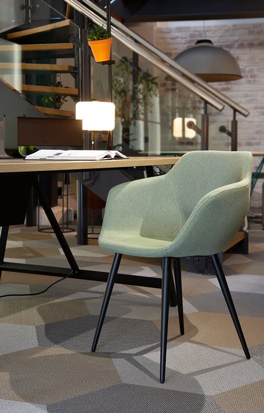 Ora Chair with an upholstered shell and 4 leg black metal base shown by a desk in an office