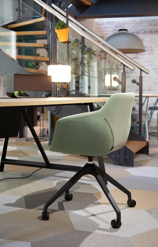 Ora Chair with an upholstered shell and 4 star swivel base on castors shown by a desk in an office