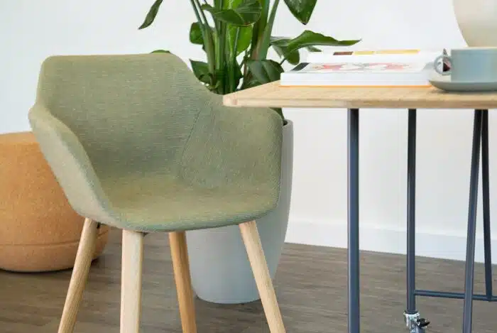 Ora Chair with an upholstered shell and wooden 4 leg base shown by a desk