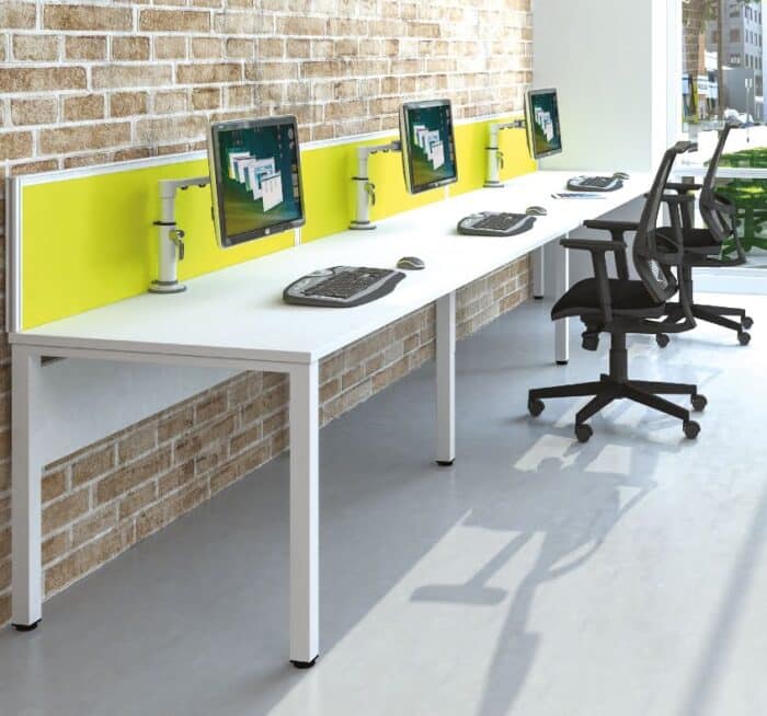 Pure Bench Desk 3 person single run with modesty panels and desk screen shown against a wall in an office space
